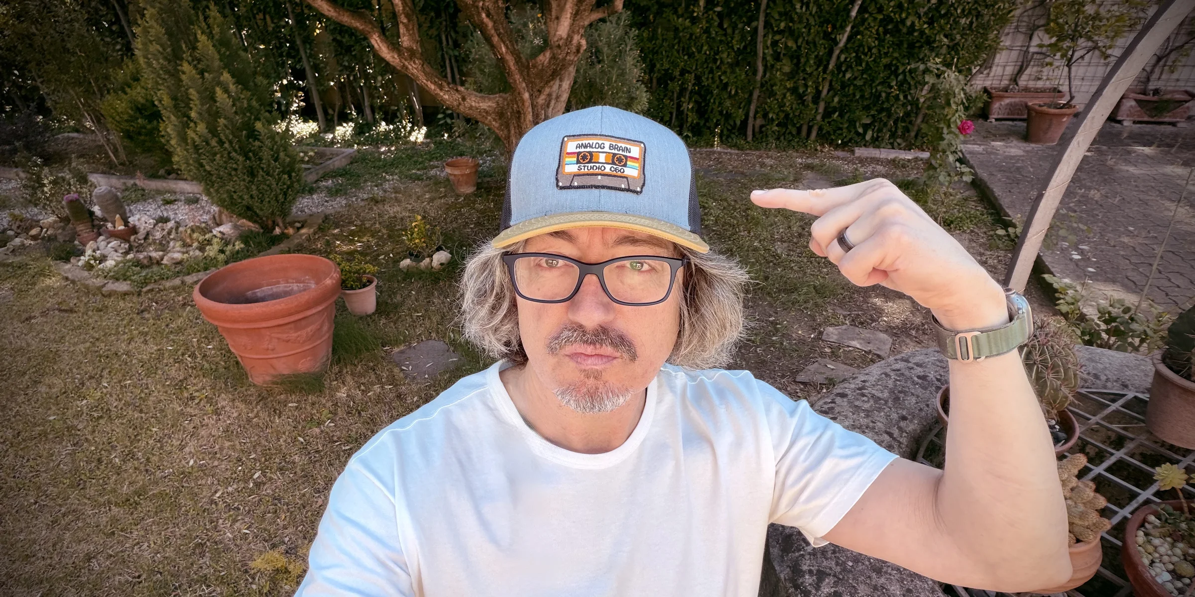Marco Ciappelli in a garden in Florence, pointing at his Analog Brain Studio C60 cap